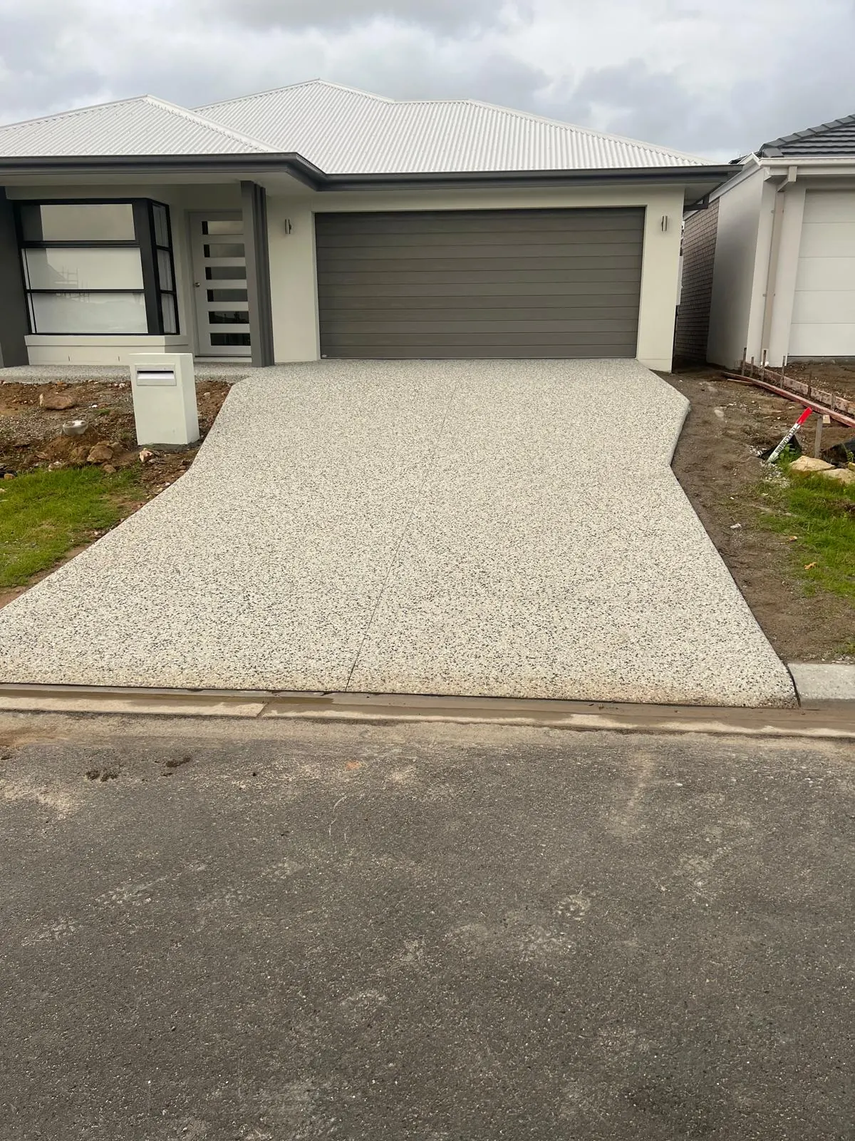 Wide exposed aggregate driveway with clean edges in front of a new Brisbane home