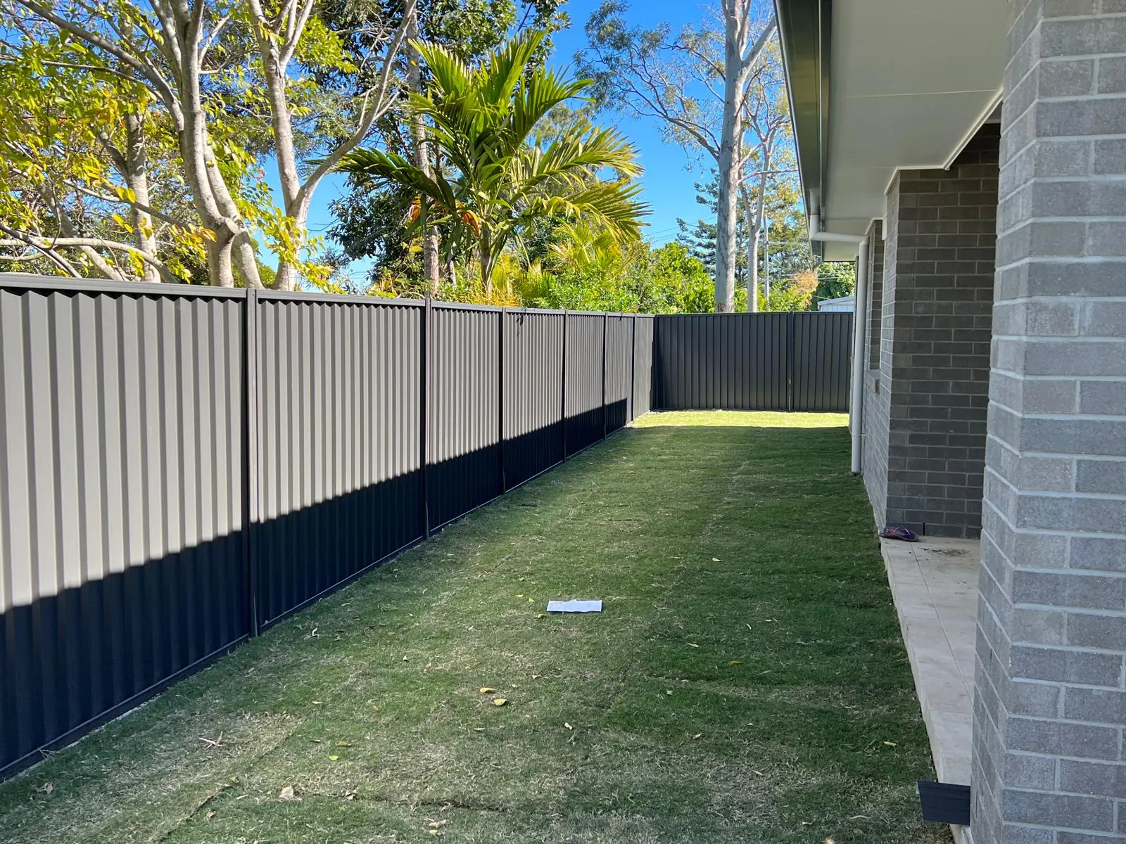 Two-tone Colorbond steel fence beside a Brisbane brick home and lawn