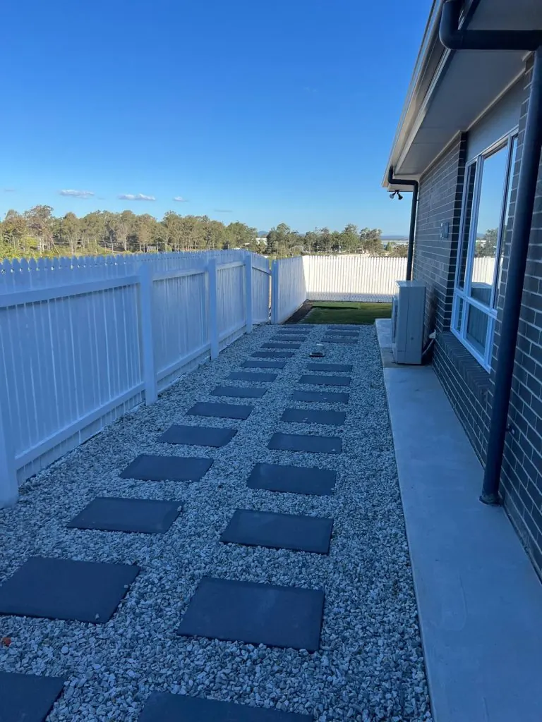 Charcoal stepping stone path through white pebbles between white fence and brick home in Brisbane